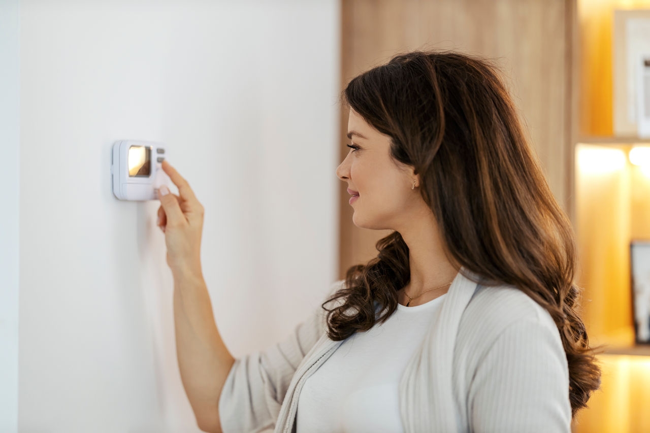 A woman operates a thermostat inside a home