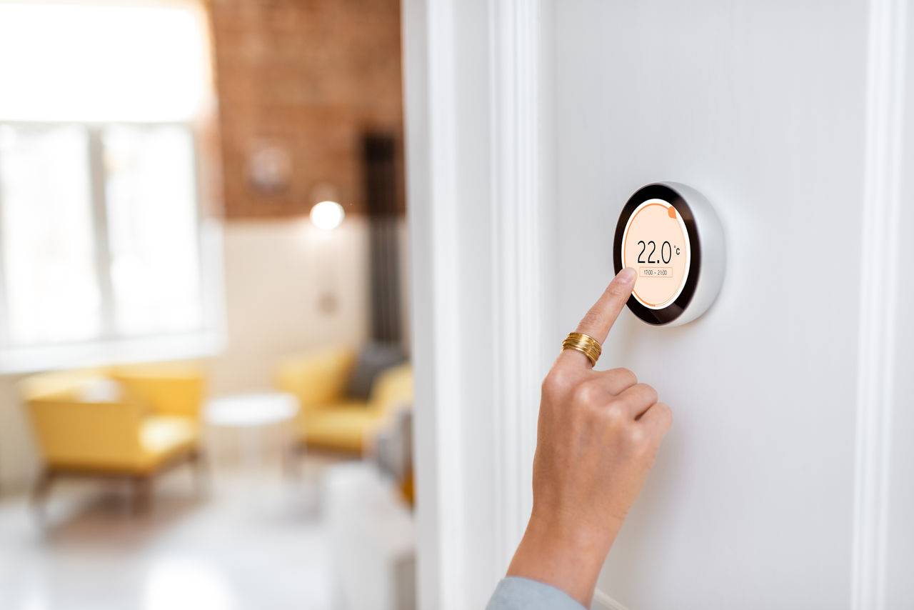 A woman adjusts a digital thermostat in a home to regulate the temperature