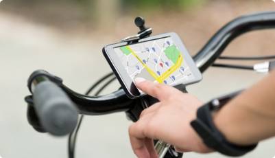 Una mano pulsa en un mapa en un móvil que está sujeto en el manillar de una bicicleta