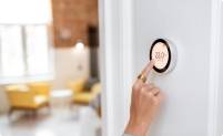 A woman adjusts a digital thermostat in a home to regulate the temperature
