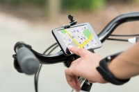 A hand taps a map on a cell phone affixed to the handlebars of a bike